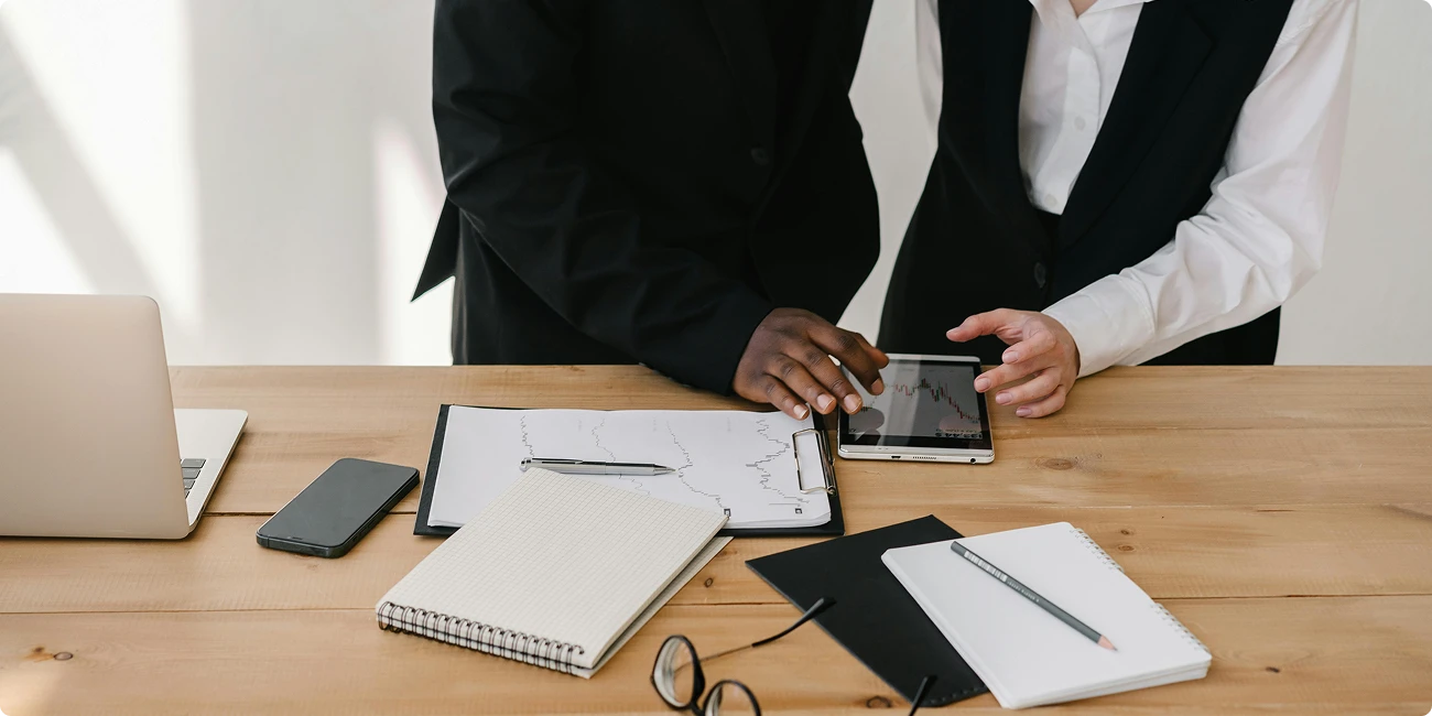 Hands signing papers at a desk with a tablet