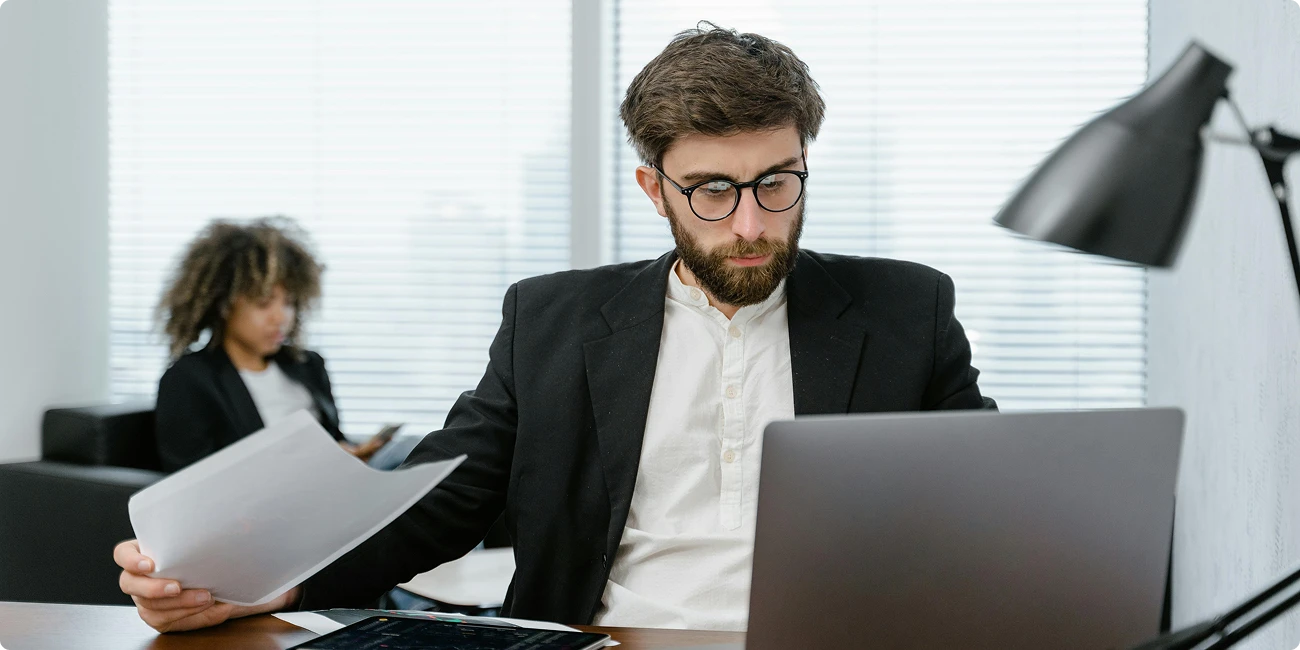 Man reading documents next to a laptop